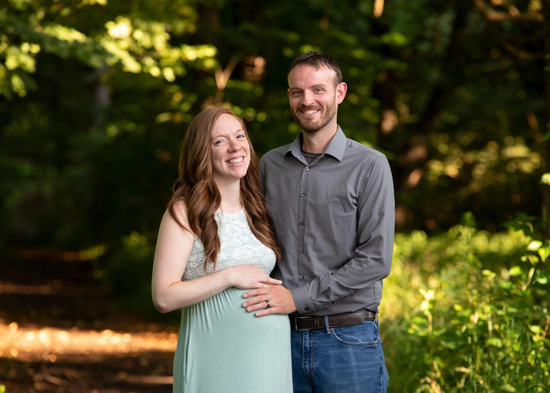 A man and a pregnant woman are posing for a picture in the woods.