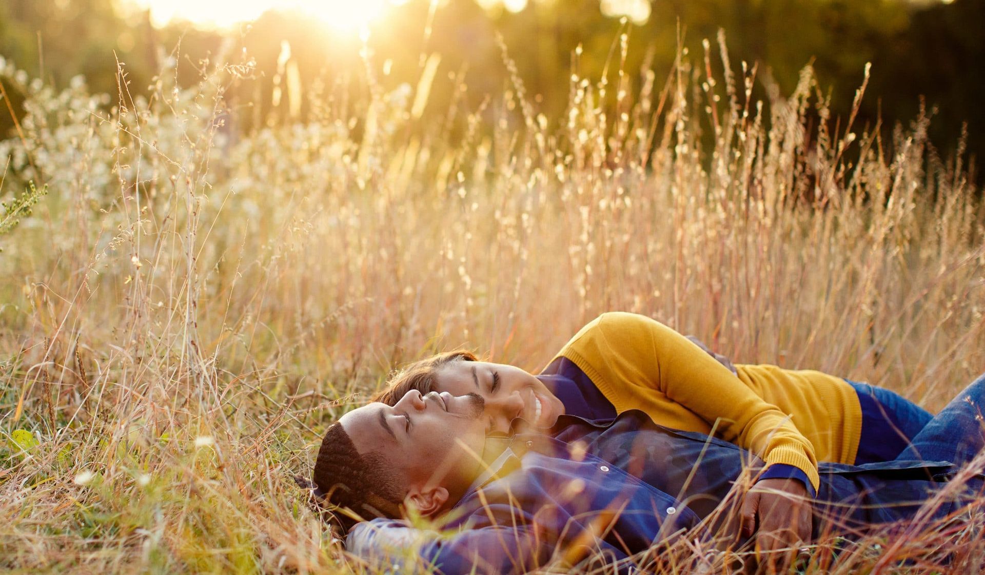 A man and a woman are laying in a field of tall grass.