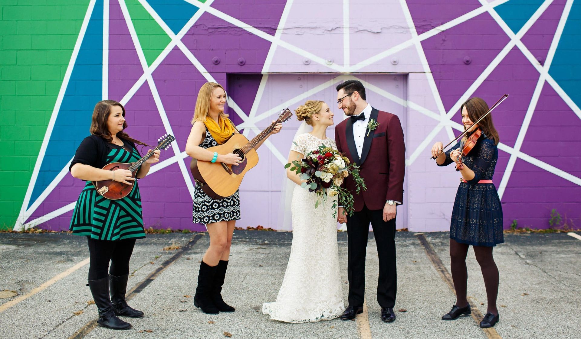 A bride and groom are standing in front of a purple wall with a group of people playing instruments.