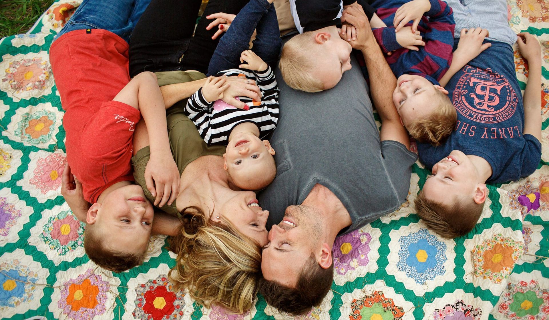 A family is laying in a circle on a blanket.