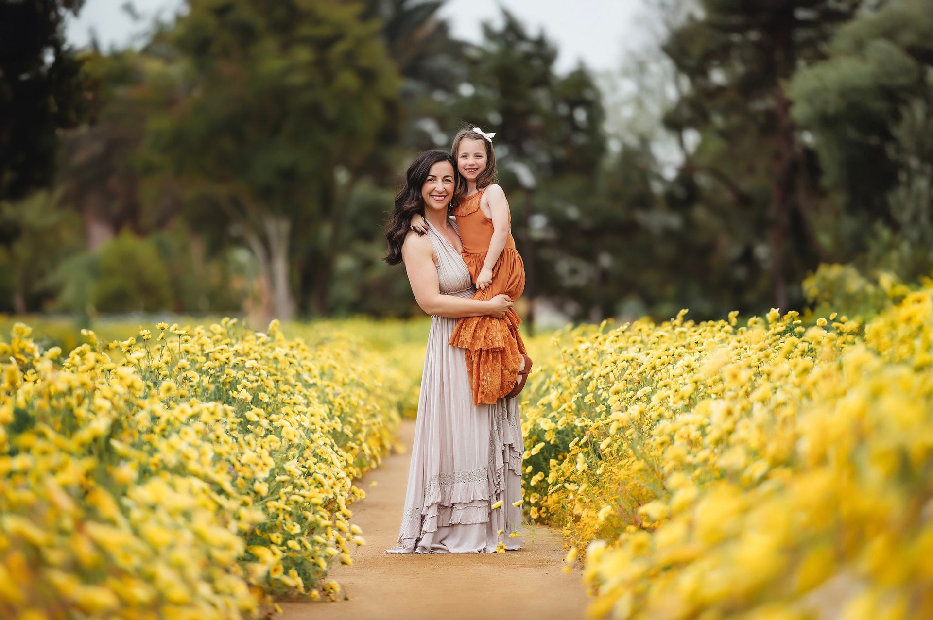 A woman and a little girl are standing in a field of yellow flowers.