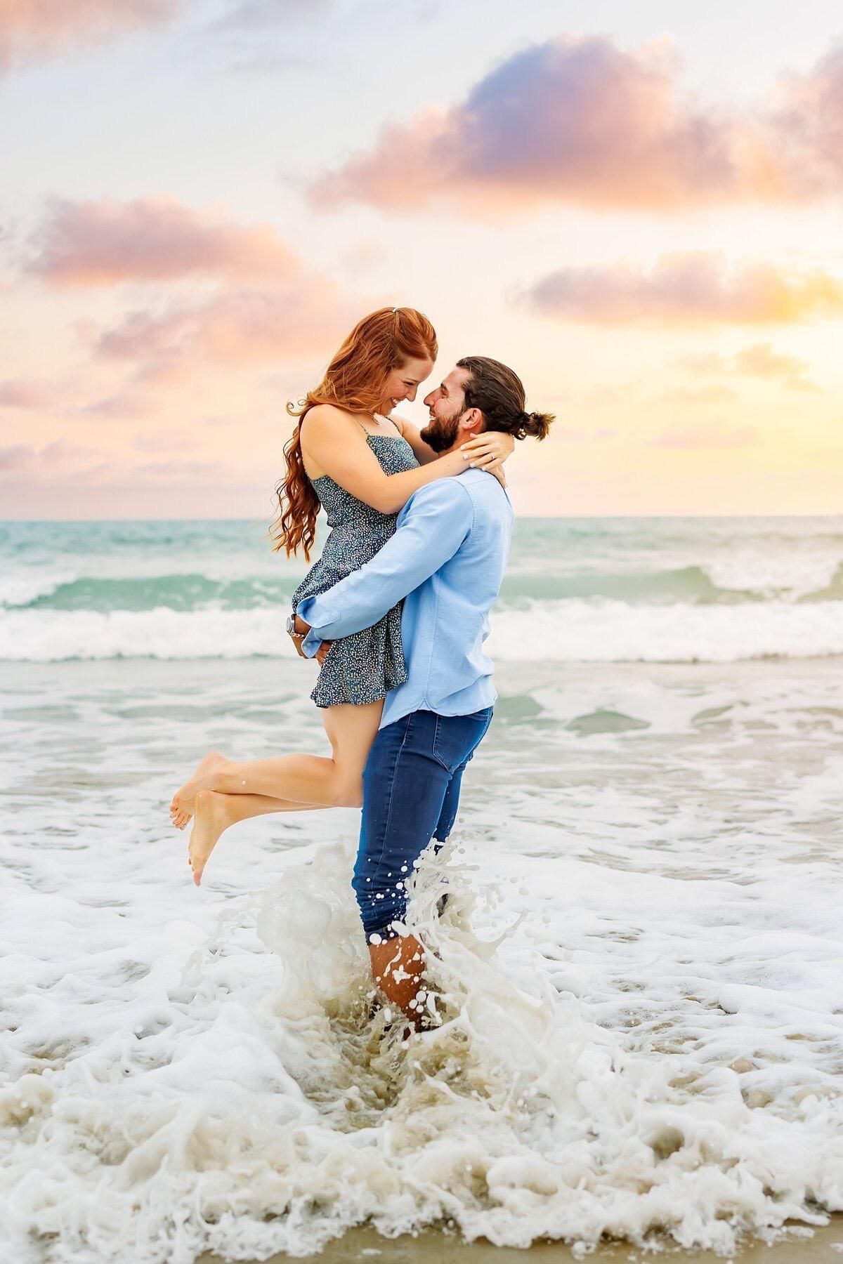 A man is holding a woman in his arms on the beach.