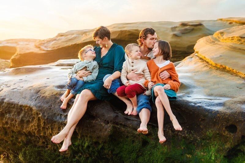 A family is sitting on a rock on the beach.