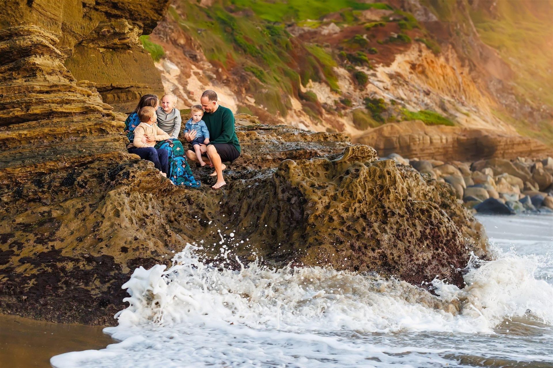 A family is sitting on a rock near the ocean.