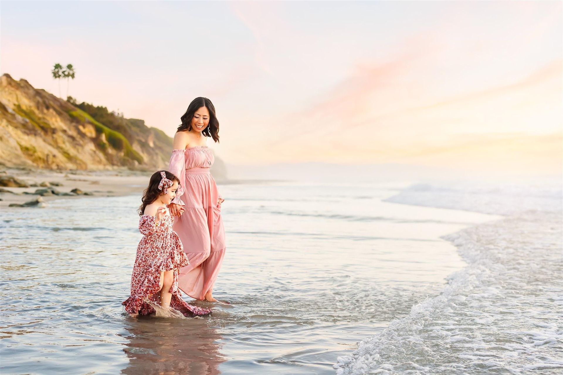 A woman and a little girl are walking on the beach.