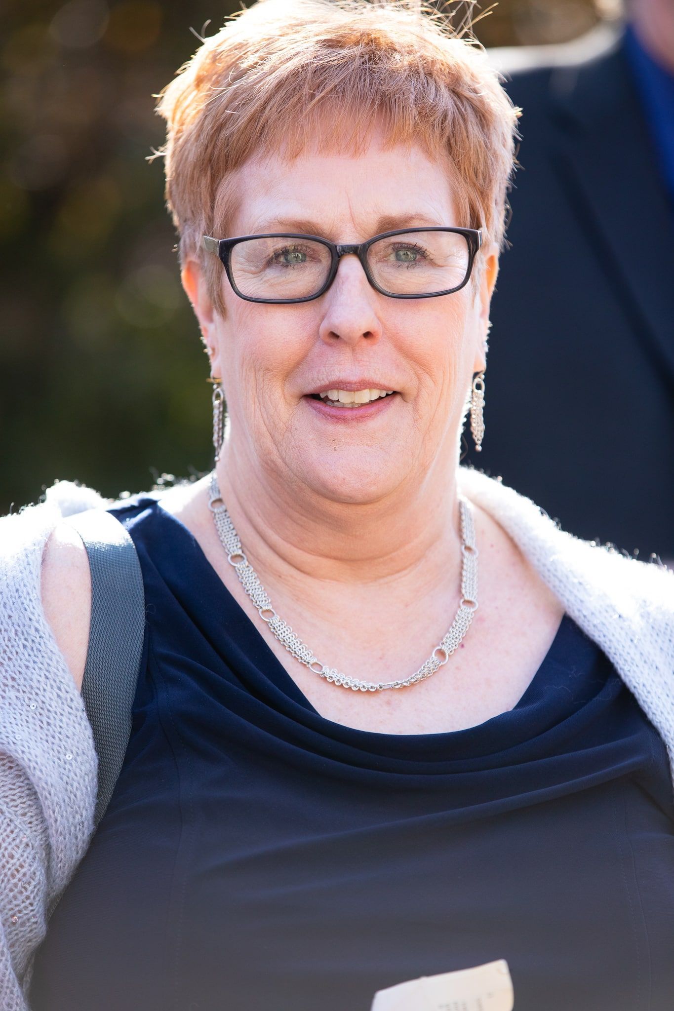 A woman wearing glasses and a necklace is smiling for the camera