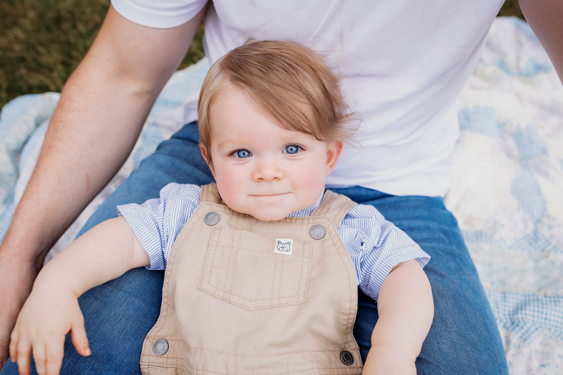 A baby is sitting on a man 's lap on a blanket.