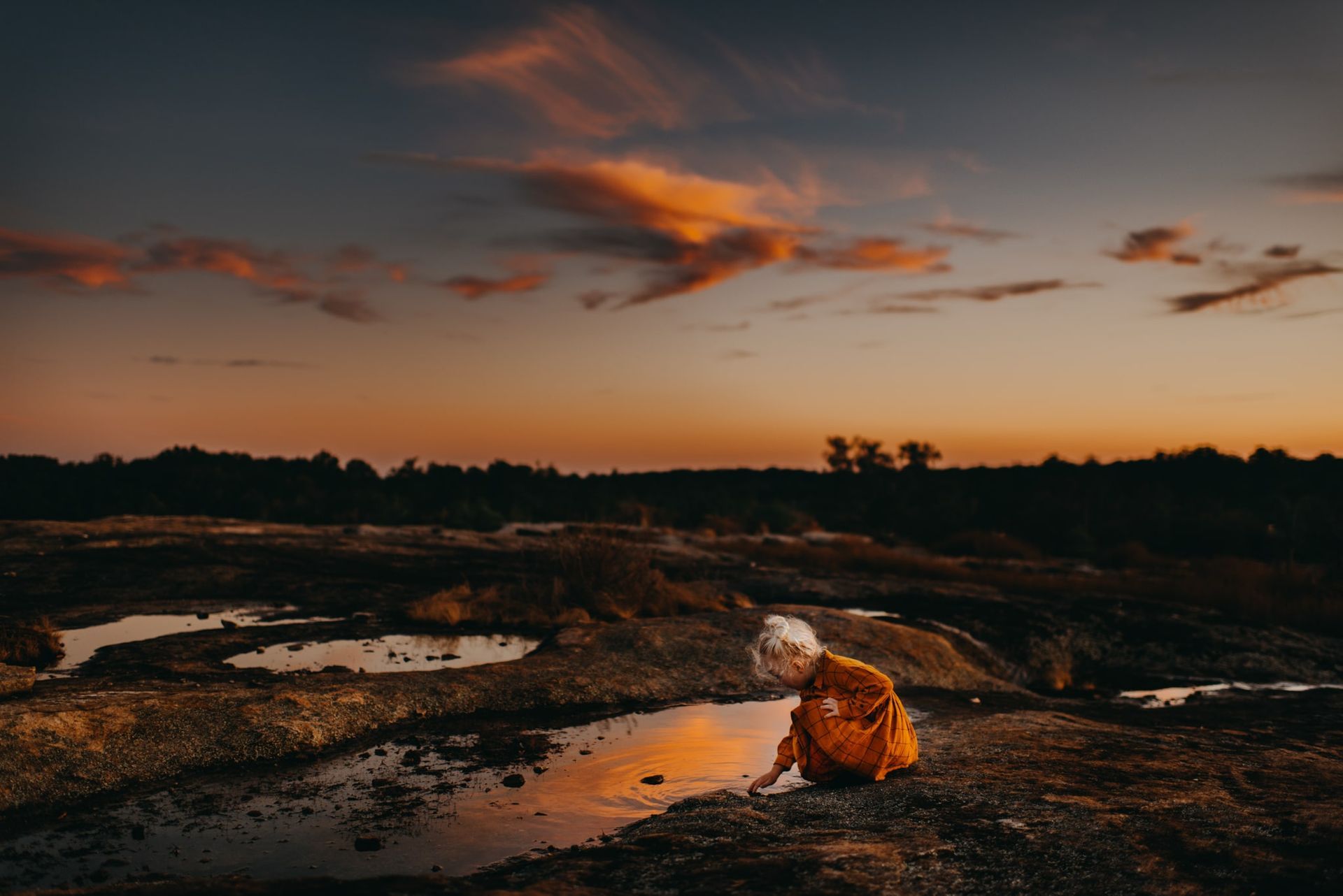 A woman is kneeling in a puddle of water at sunset.