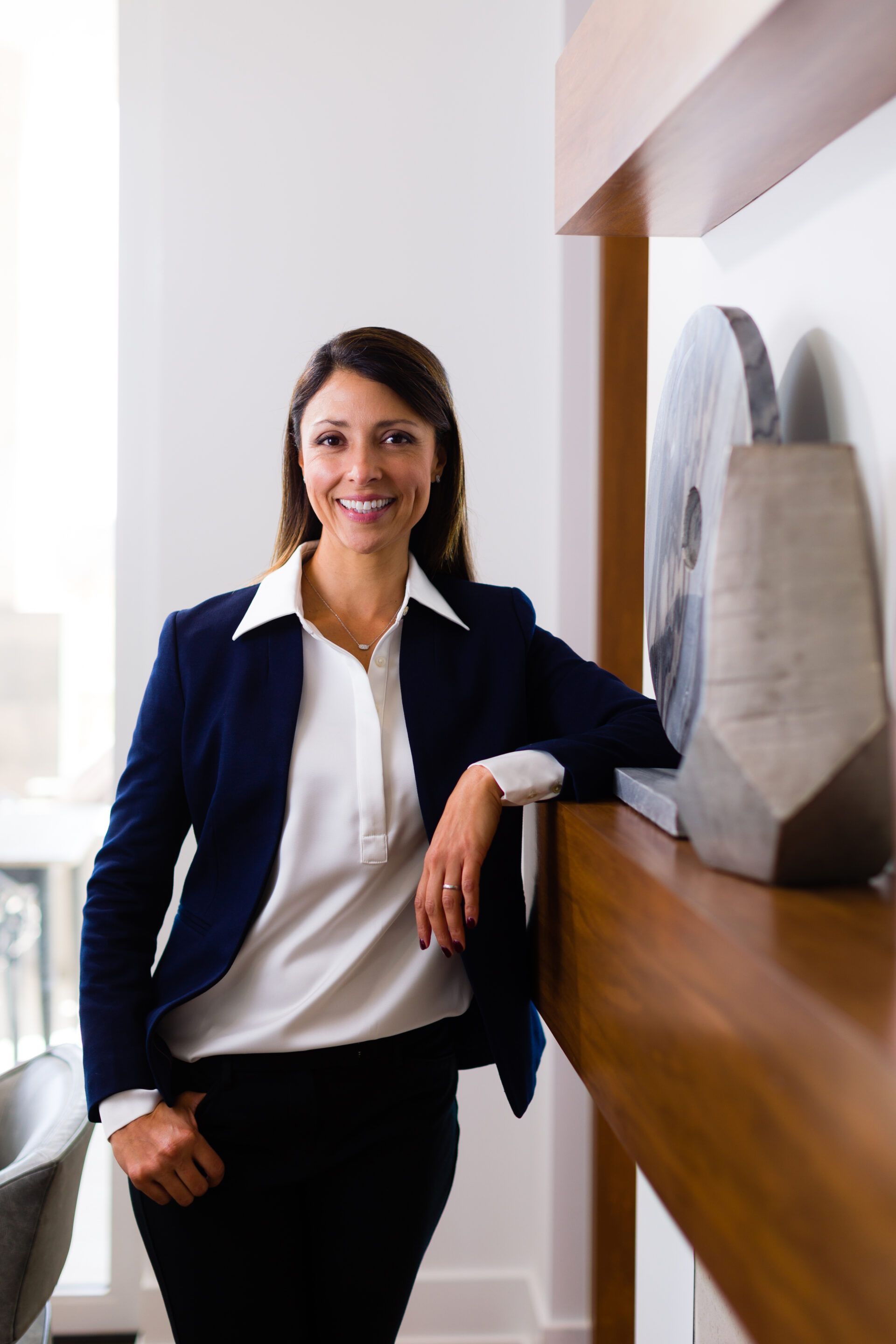 A woman in a blue jacket and white shirt is standing next to a fireplace.