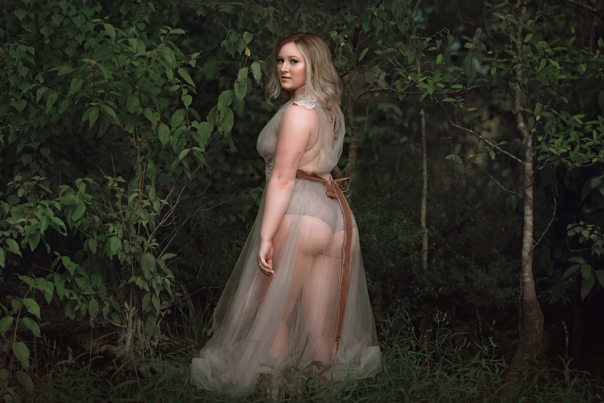 A woman in a sheer dress is standing in the woods.