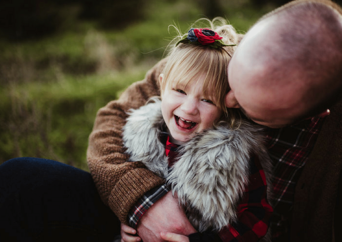 A man is holding a little girl in his arms and the little girl is laughing.