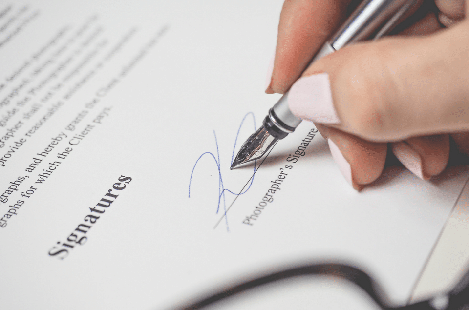 A woman is signing a document with a fountain pen.