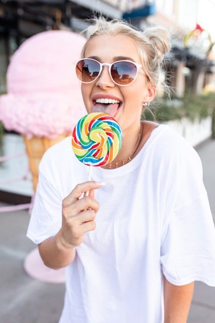 A woman wearing sunglasses is eating a colorful lollipop.