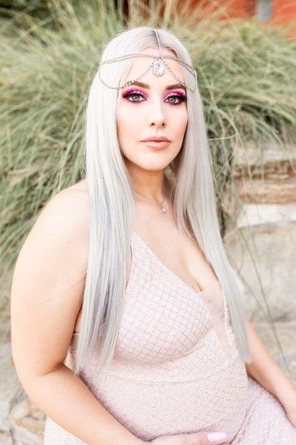 A woman with long white hair is wearing a pink dress and a headpiece.