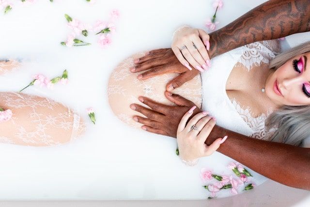 A pregnant woman is laying in a bathtub filled with milk and flowers.