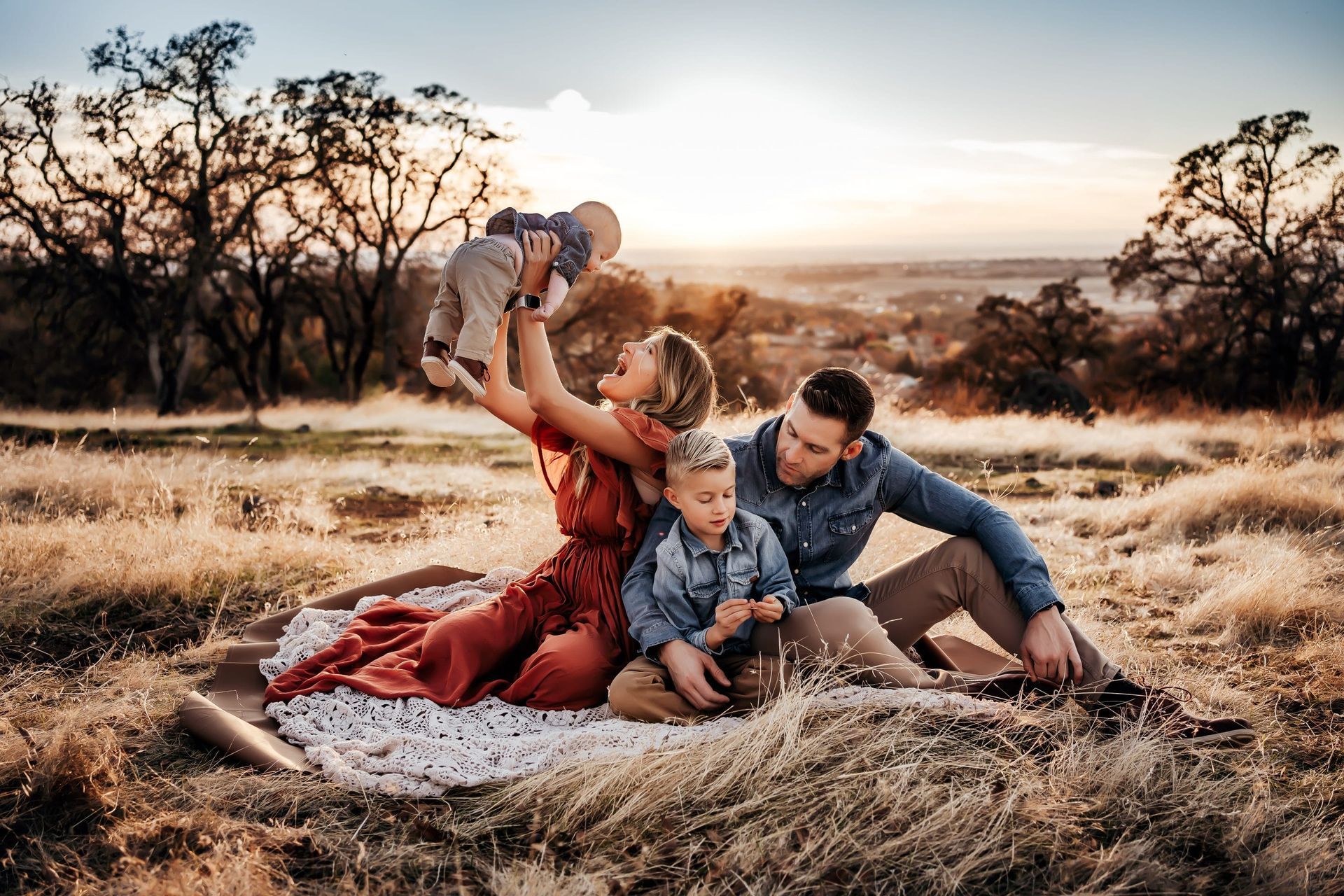 A family is sitting on a blanket in a field.