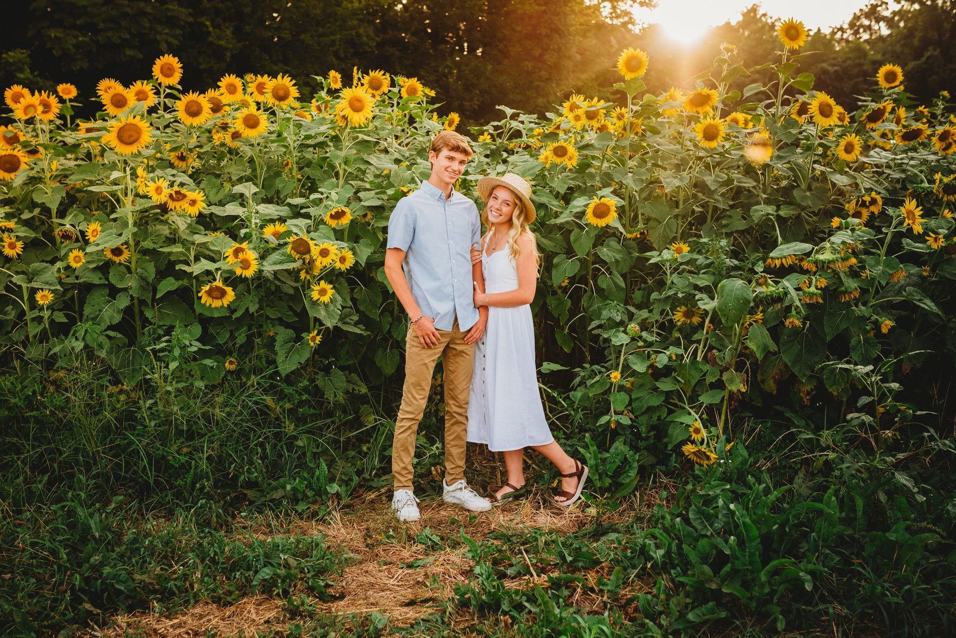 A man and a woman are standing in front of a field of sunflowers.