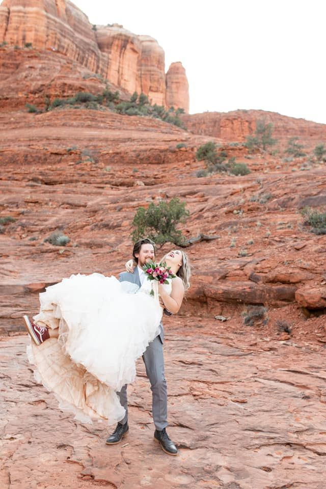 A man is carrying a bride in his arms in the desert.