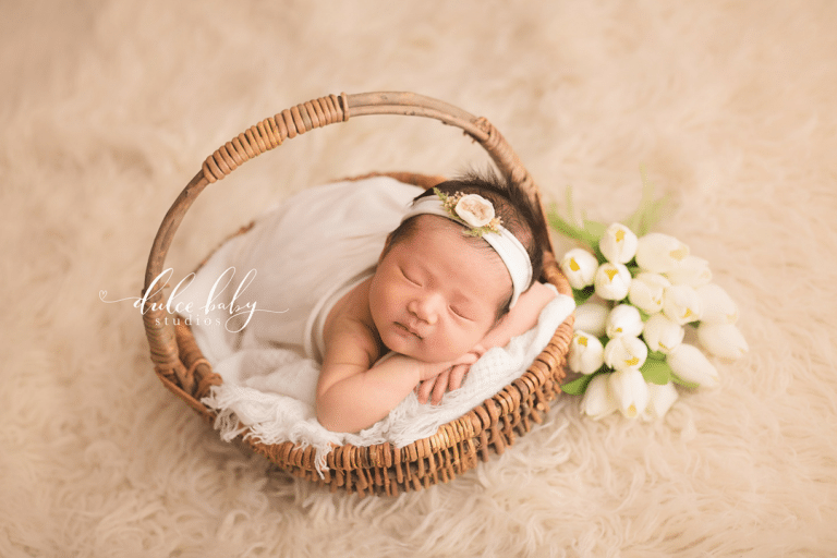 A newborn baby is sleeping in a basket with white flowers.