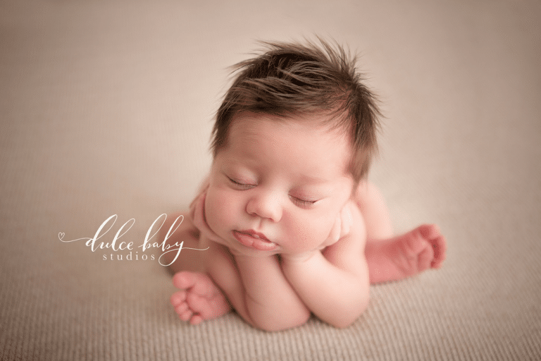 A newborn baby is laying on a blanket with his head on his hands.