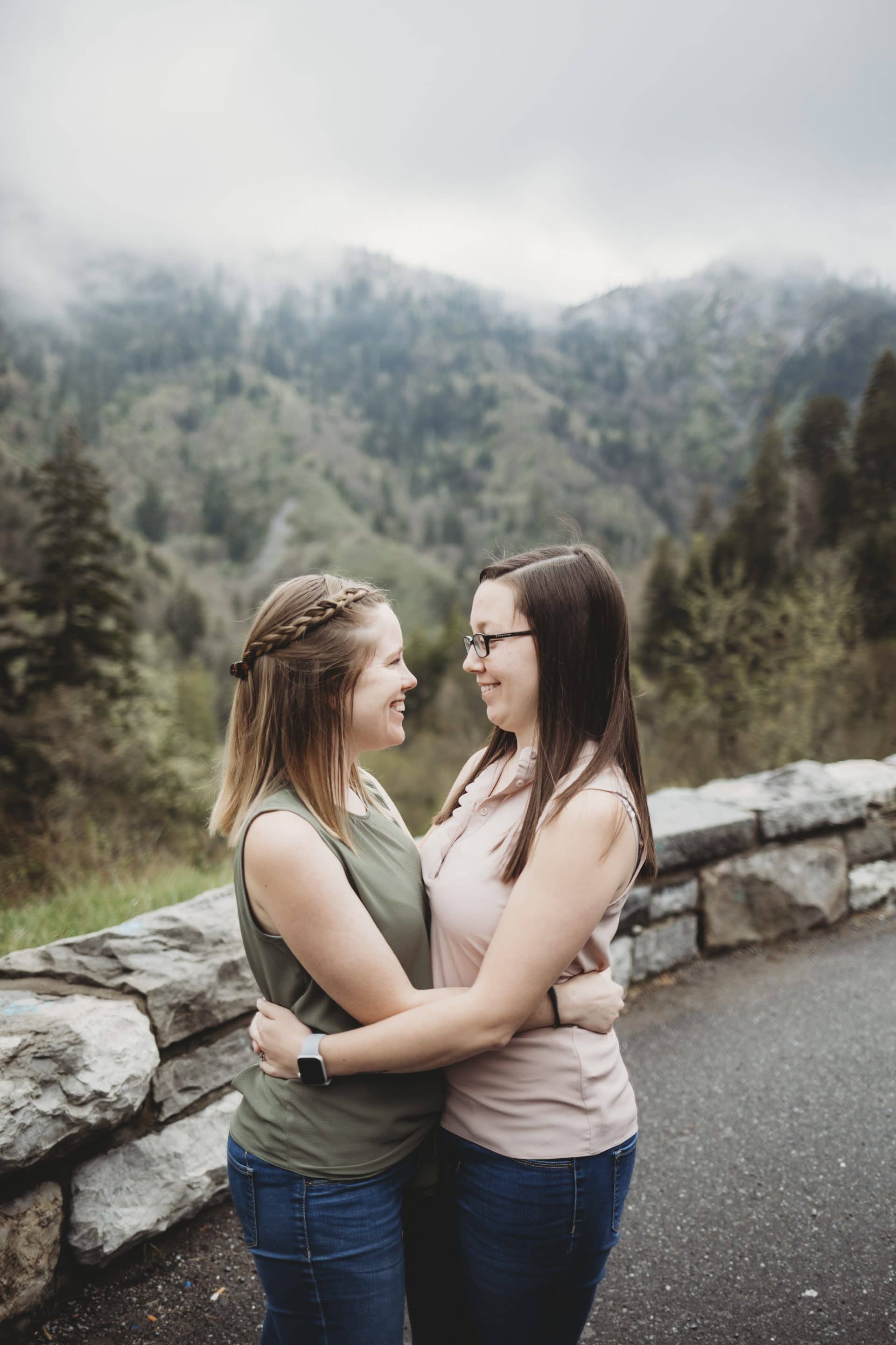 Two women are hugging each other in front of a mountain.