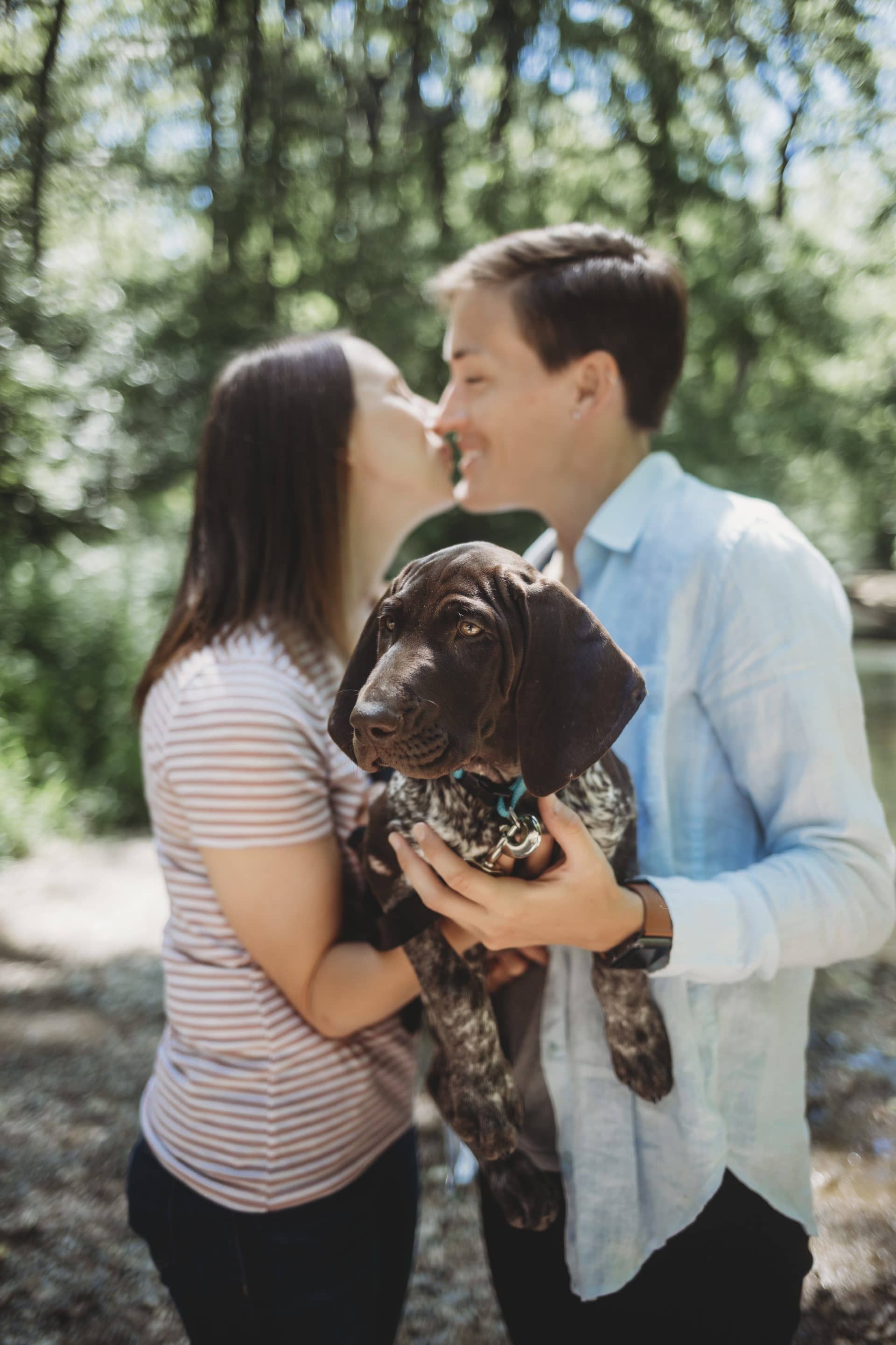 A man and a woman are kissing while holding a puppy in their arms.