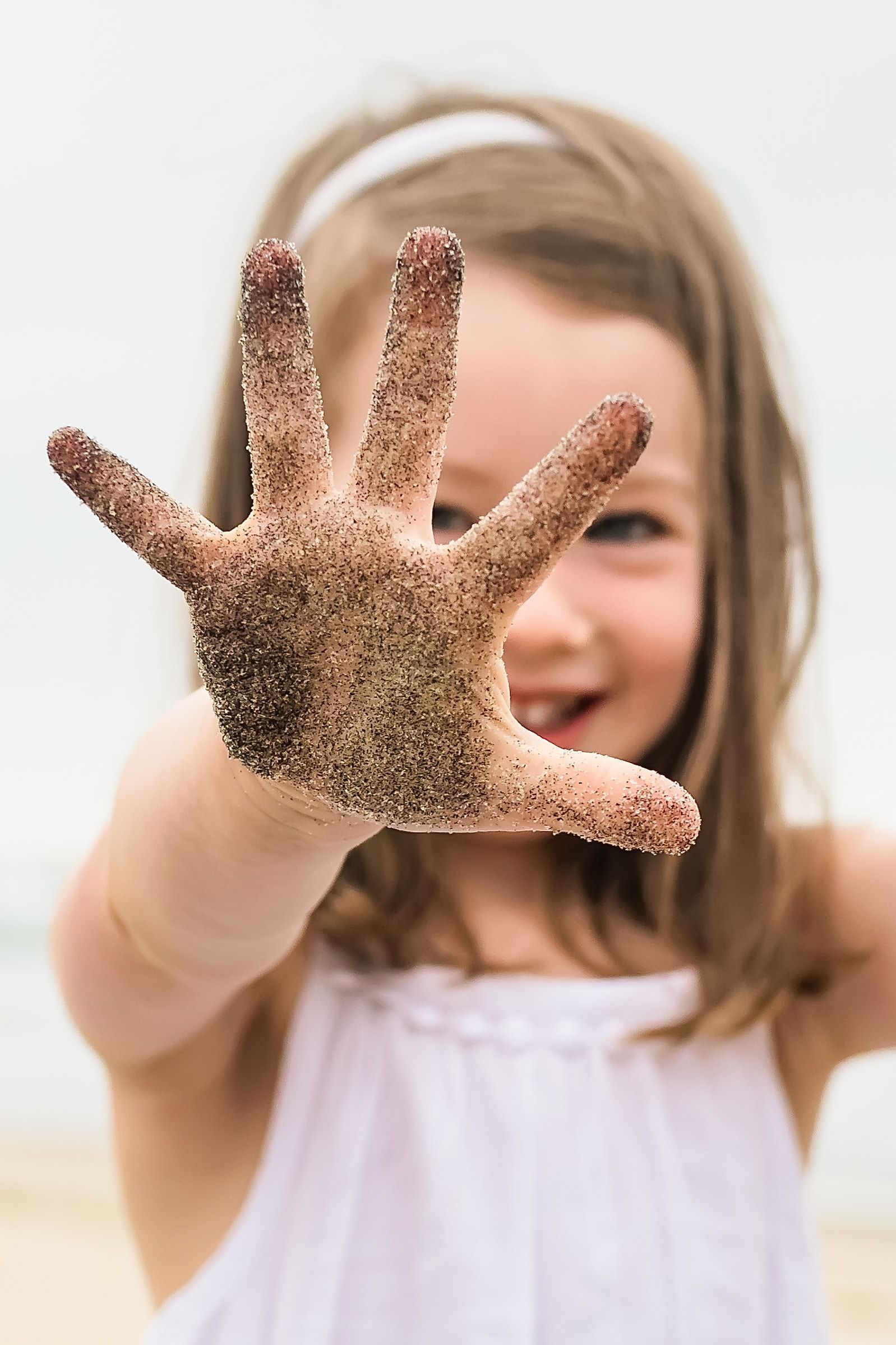 A little girl is holding up her hand covered in sand.