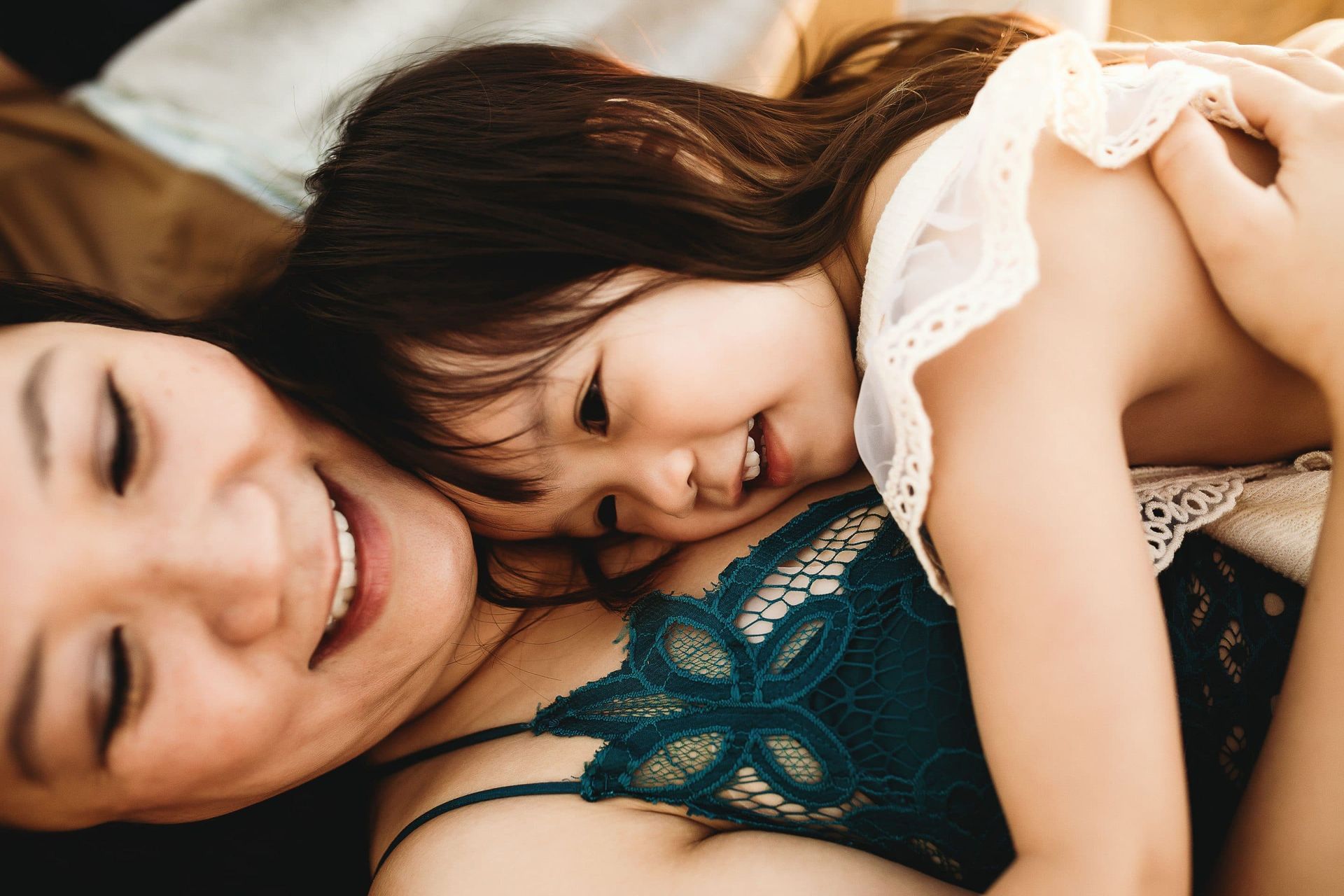 A woman is laying on a bed holding a little girl who is smiling.