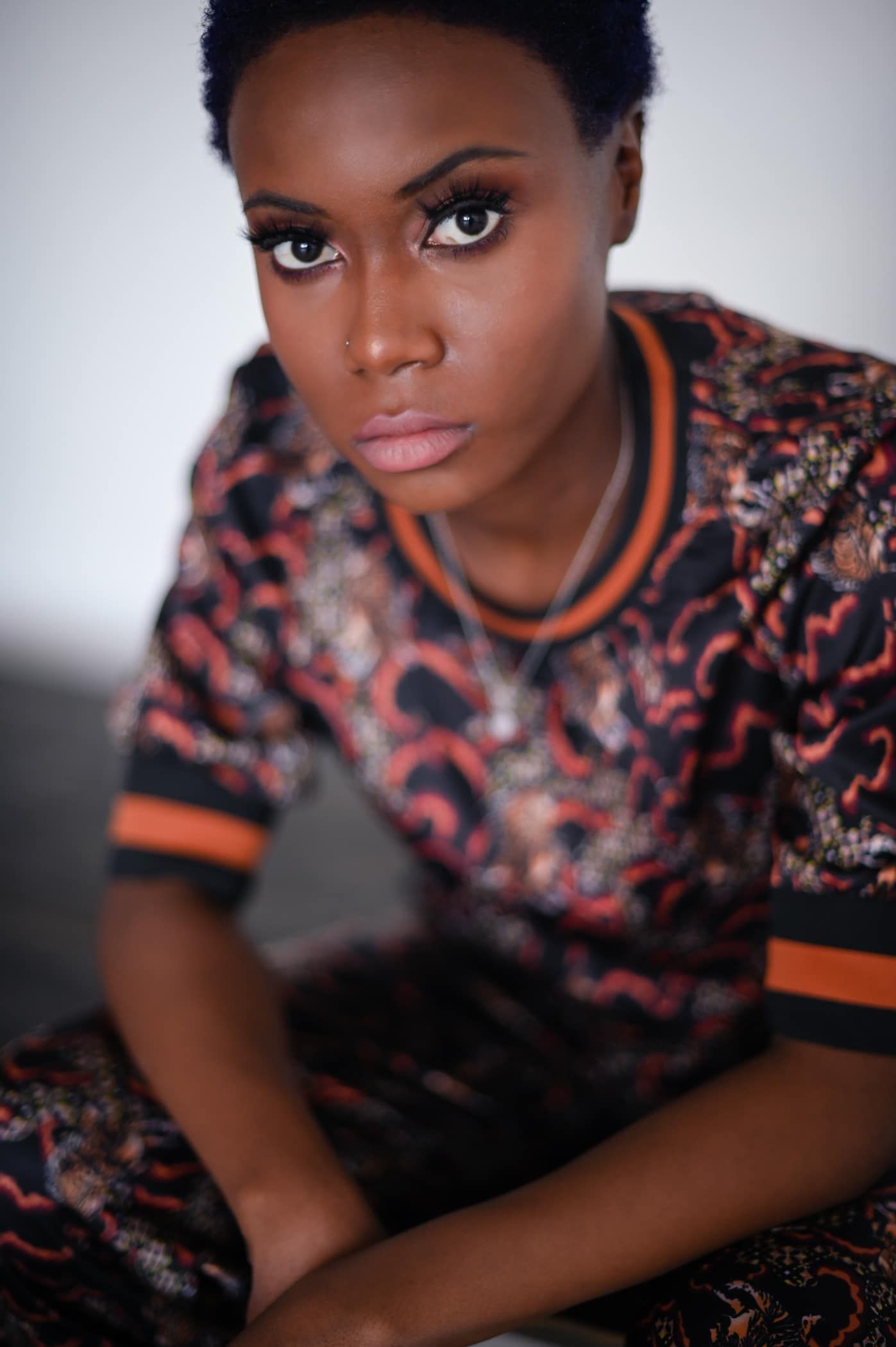 A woman is sitting on the floor wearing a colorful shirt and looking at the camera.