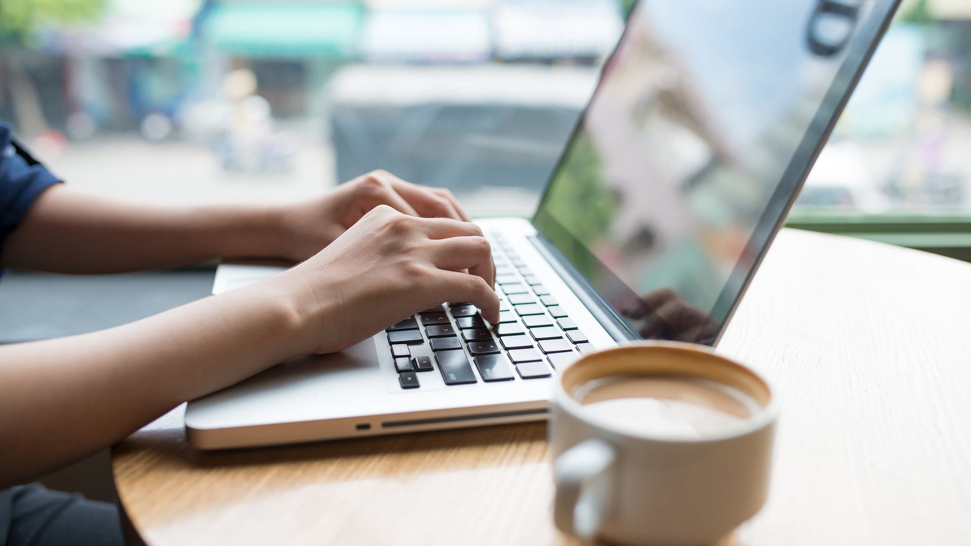 A person is typing on a laptop computer next to a cup of coffee.