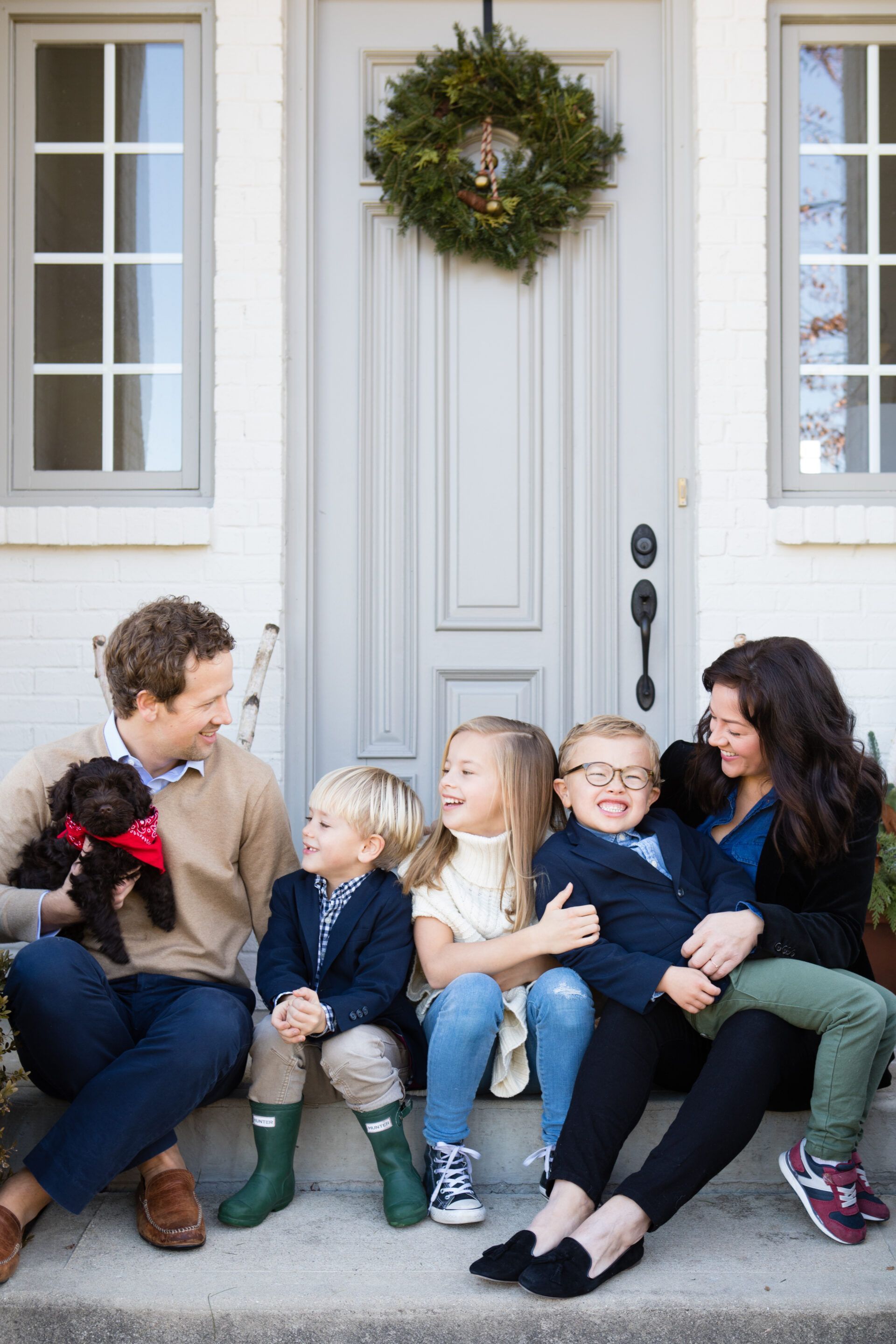 A family is sitting on the steps of a house with a dog.