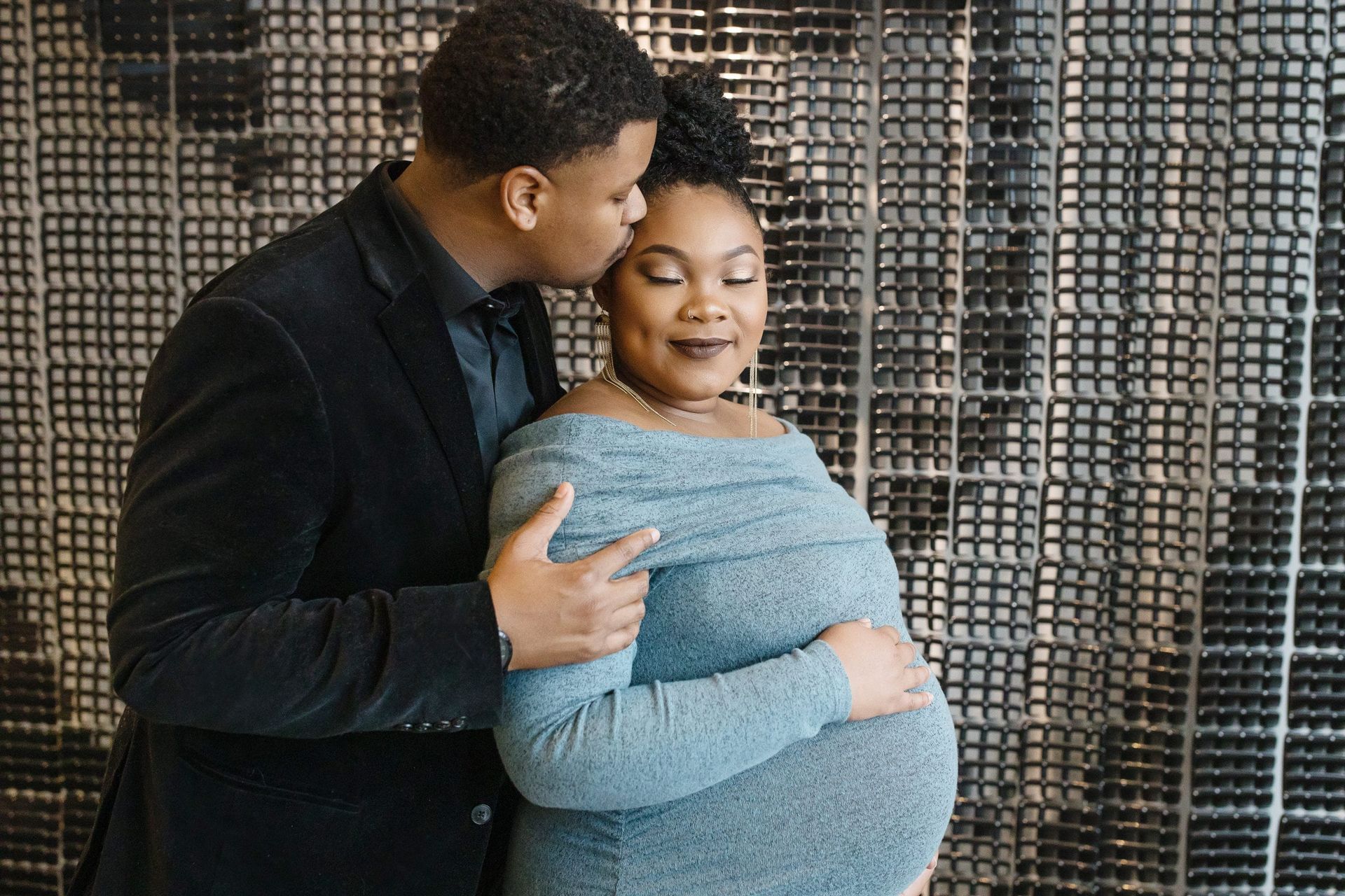 A man is kissing a pregnant woman on the cheek.