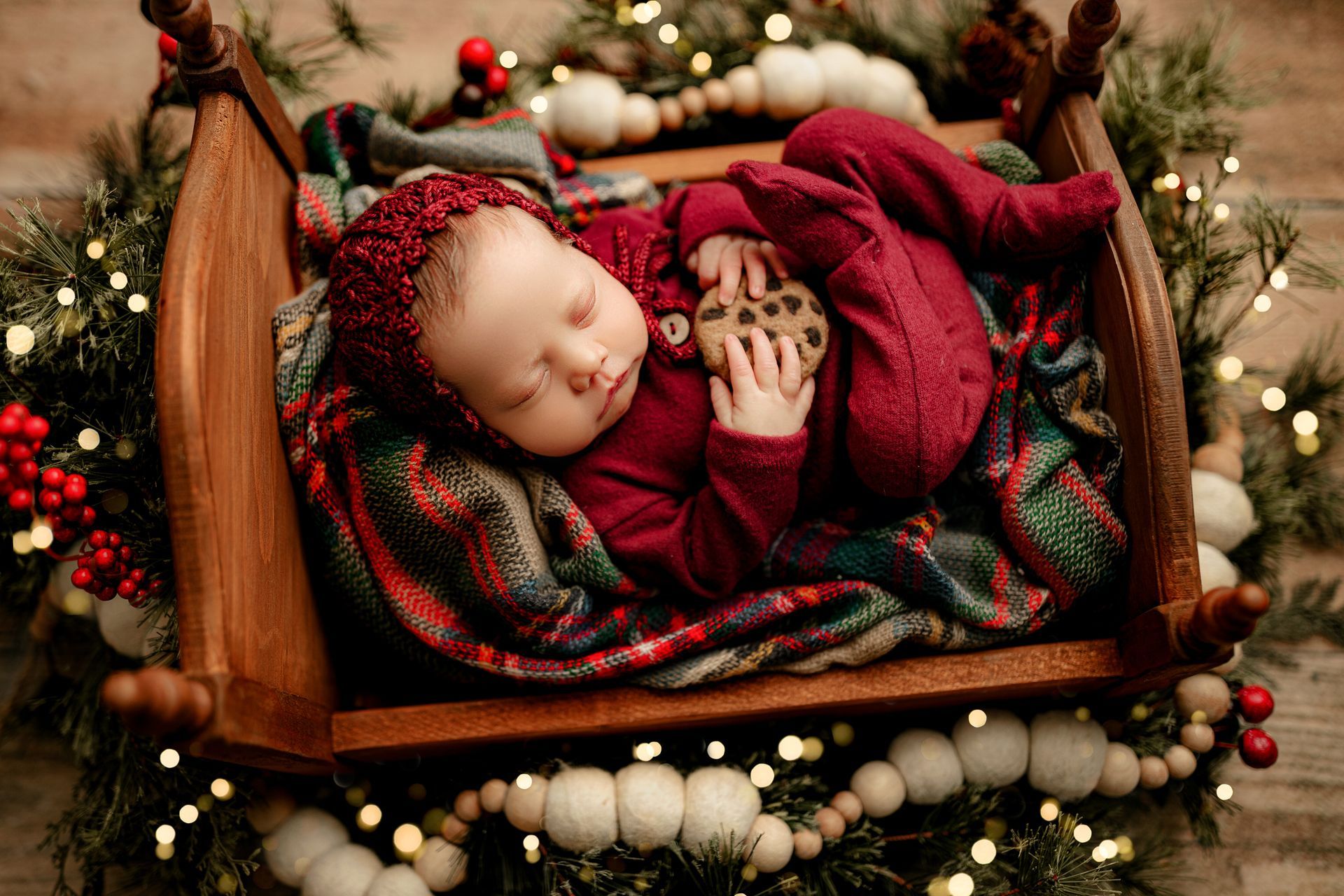 A newborn baby is sleeping in a wooden bed surrounded by christmas decorations.