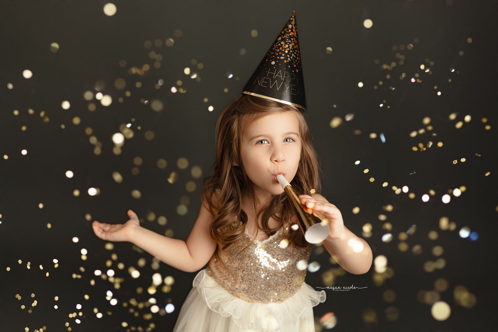 A little girl in a party hat is blowing a party horn.