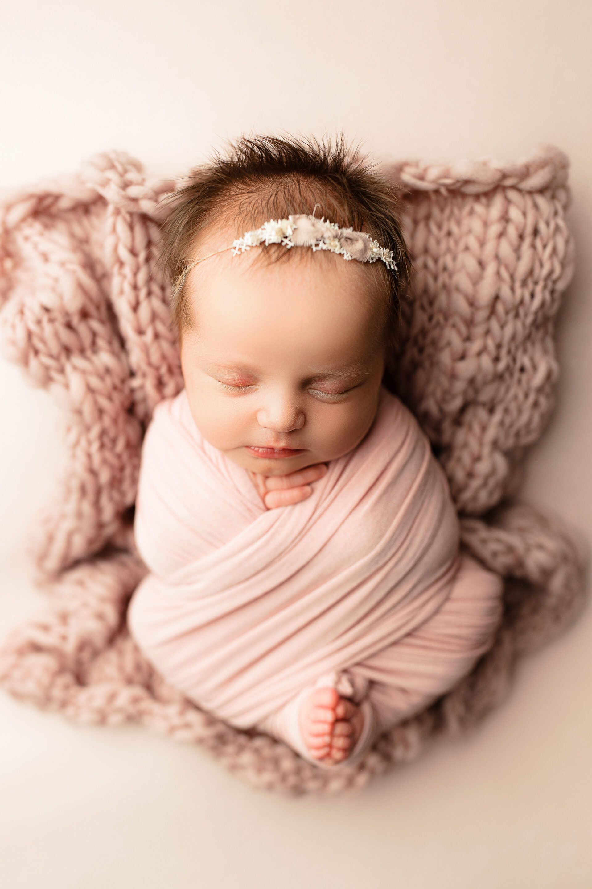 A newborn baby wrapped in a pink blanket is sleeping on a pink blanket.