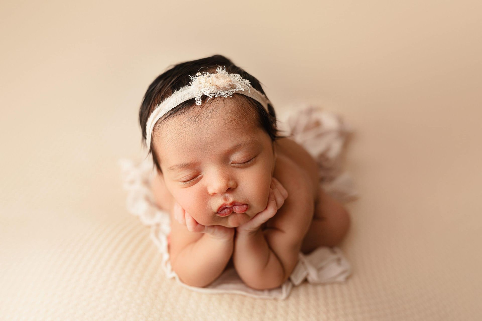 A newborn baby girl is laying on her stomach with her head on her hands.