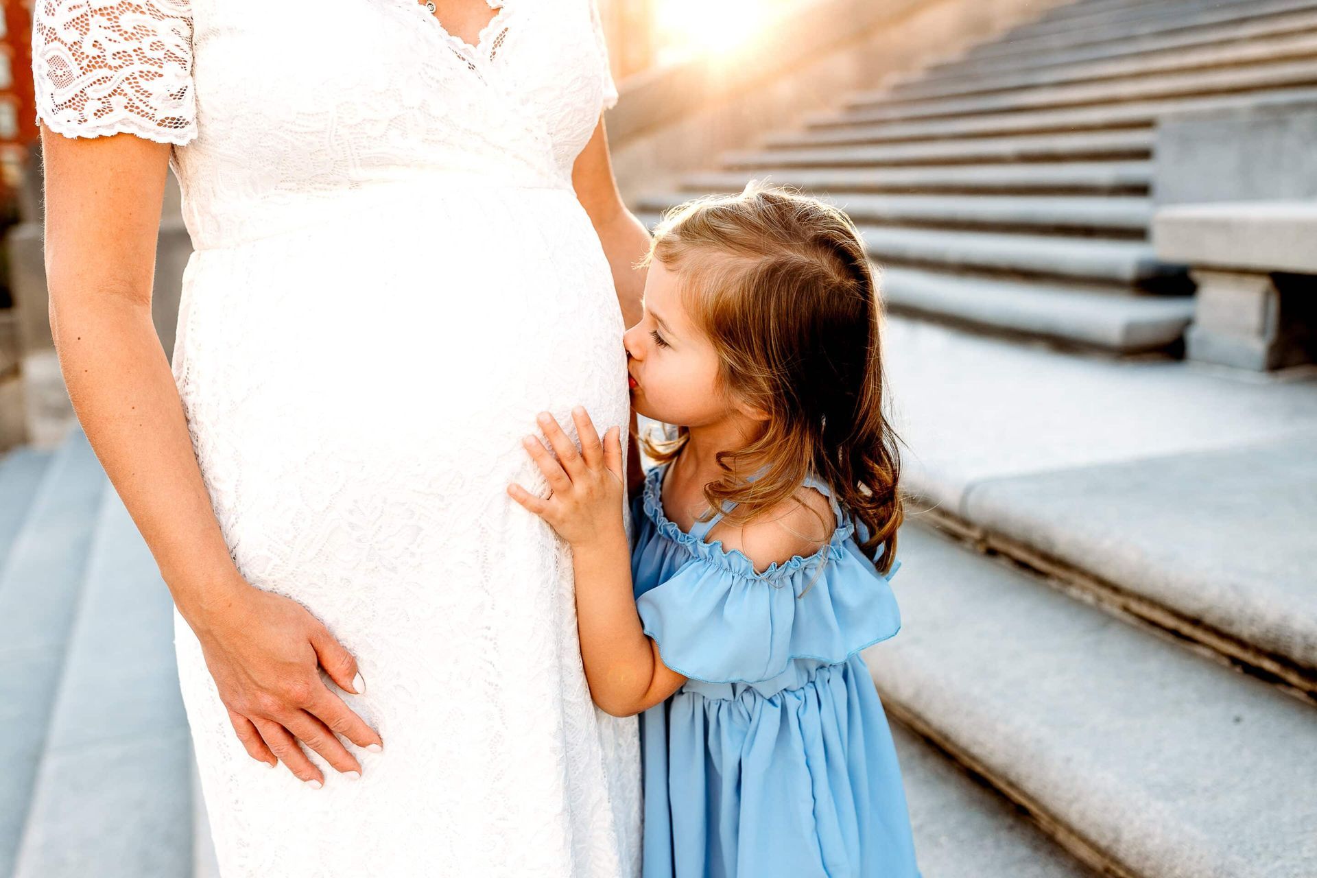 A little girl kissing her mother's pregnant stomach. 