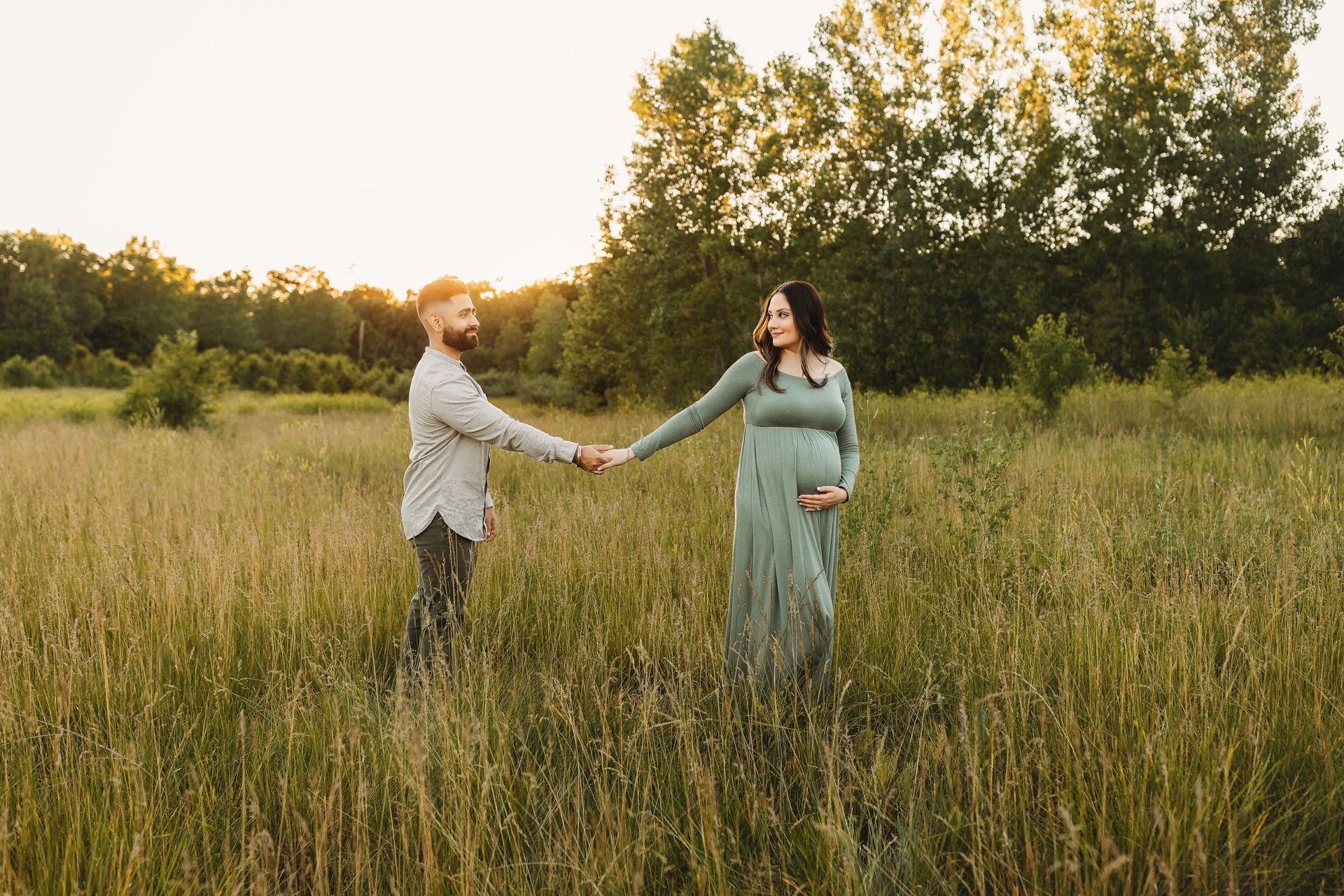 A man and a pregnant woman are holding hands in a field.