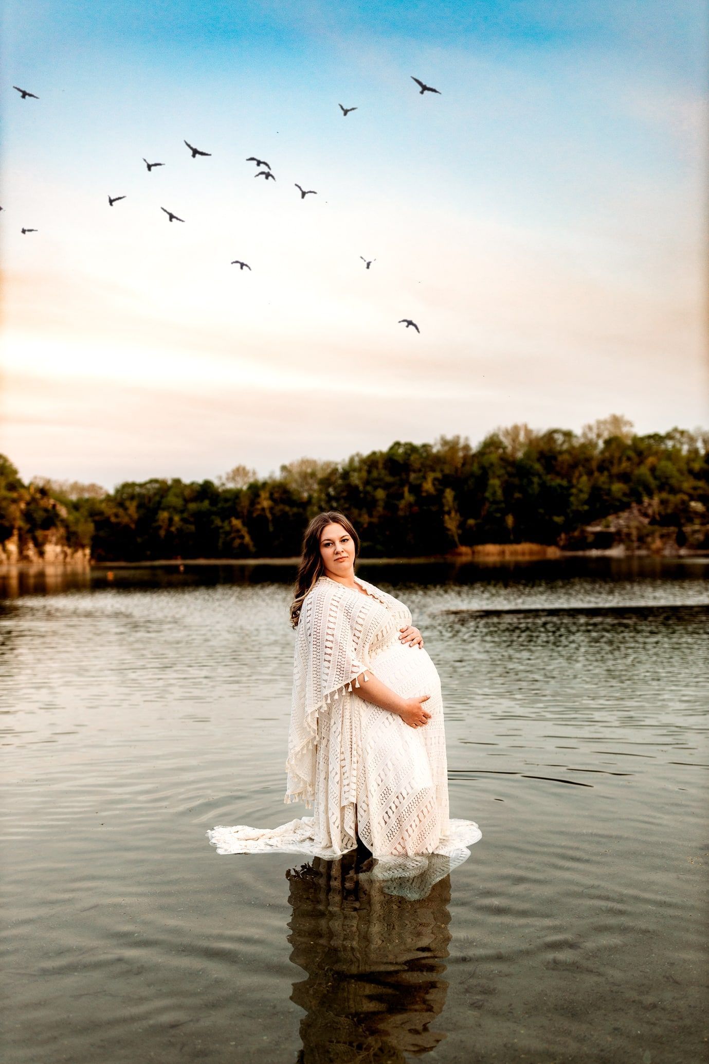 A pregnant woman in a white dress is standing in the water.