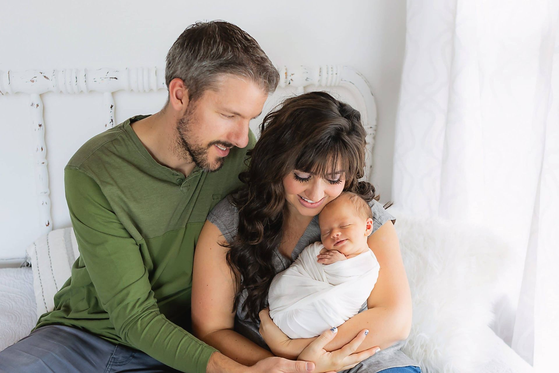 A man and woman are sitting on a bed holding a newborn baby.