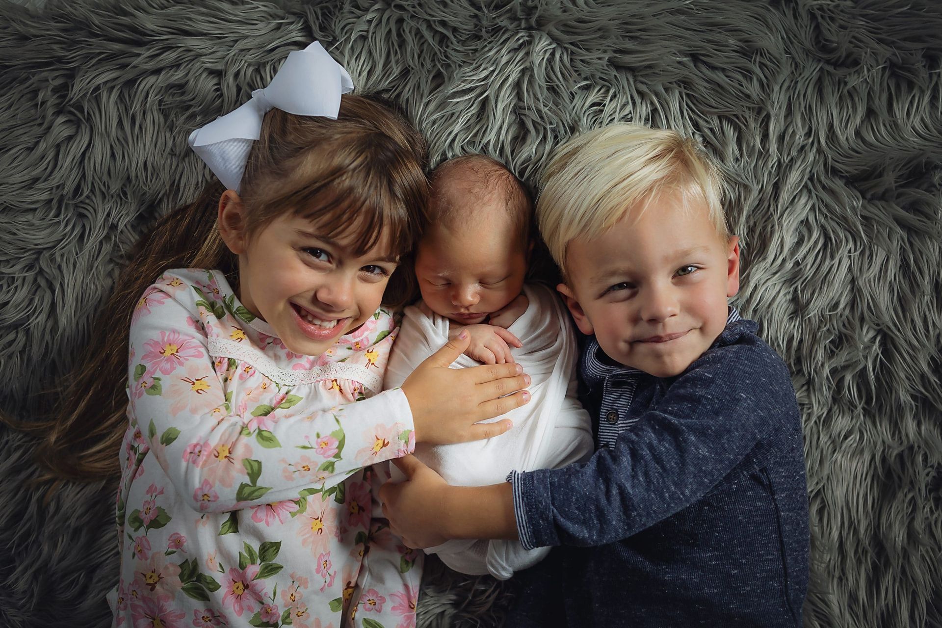 A girl and two boys are holding a newborn baby.