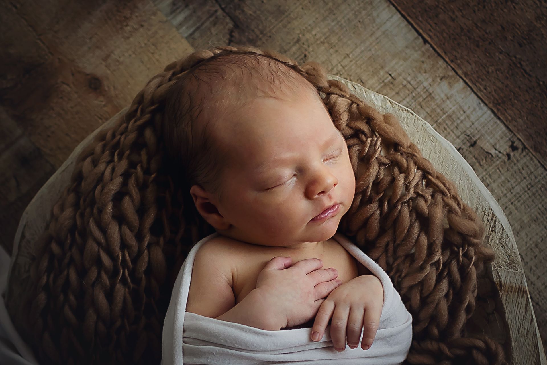 A newborn baby wrapped in a white blanket is sleeping in a basket.