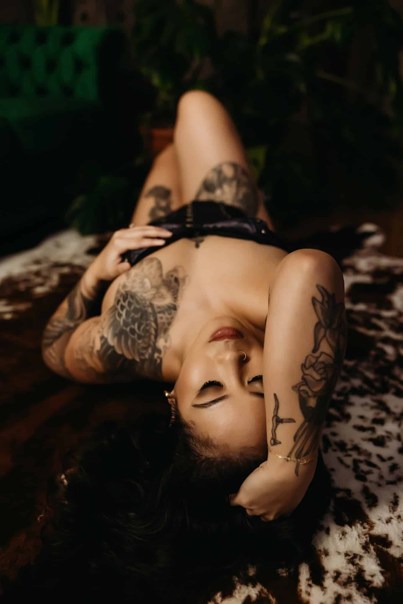 A woman with tattoos is laying on a cowhide rug.