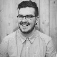 A man with a beard and glasses is smiling in a black and white photo.