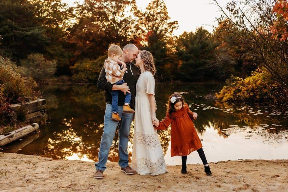 A family is posing for a picture on the beach near a lake.