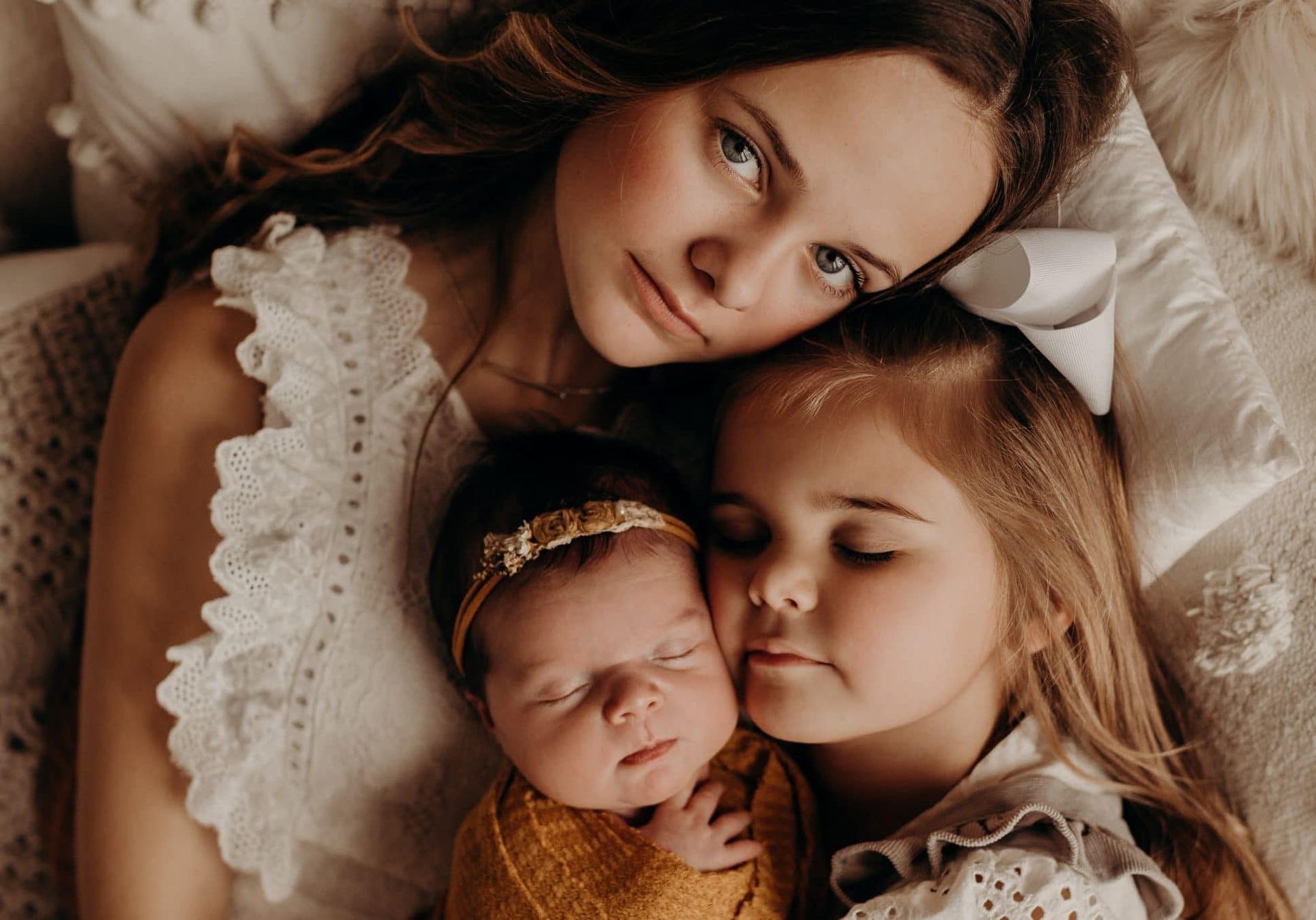 A woman is laying on a bed with two little girls and a newborn baby.