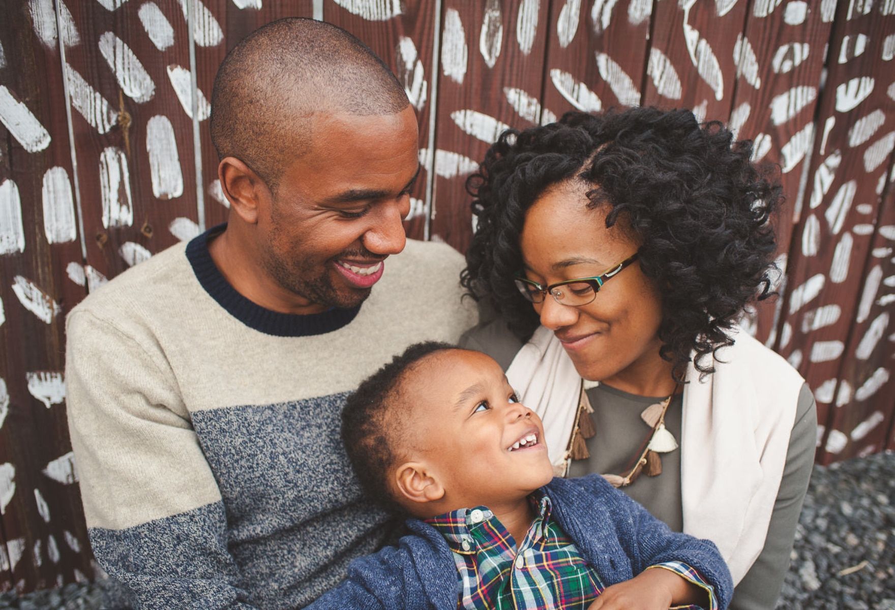 A family is sitting next to each other in front of a wooden wall.