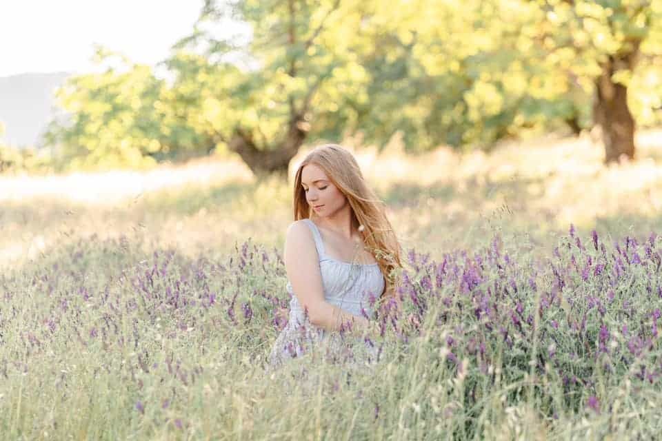 A woman in a white dress is standing in a field of purple flowers.