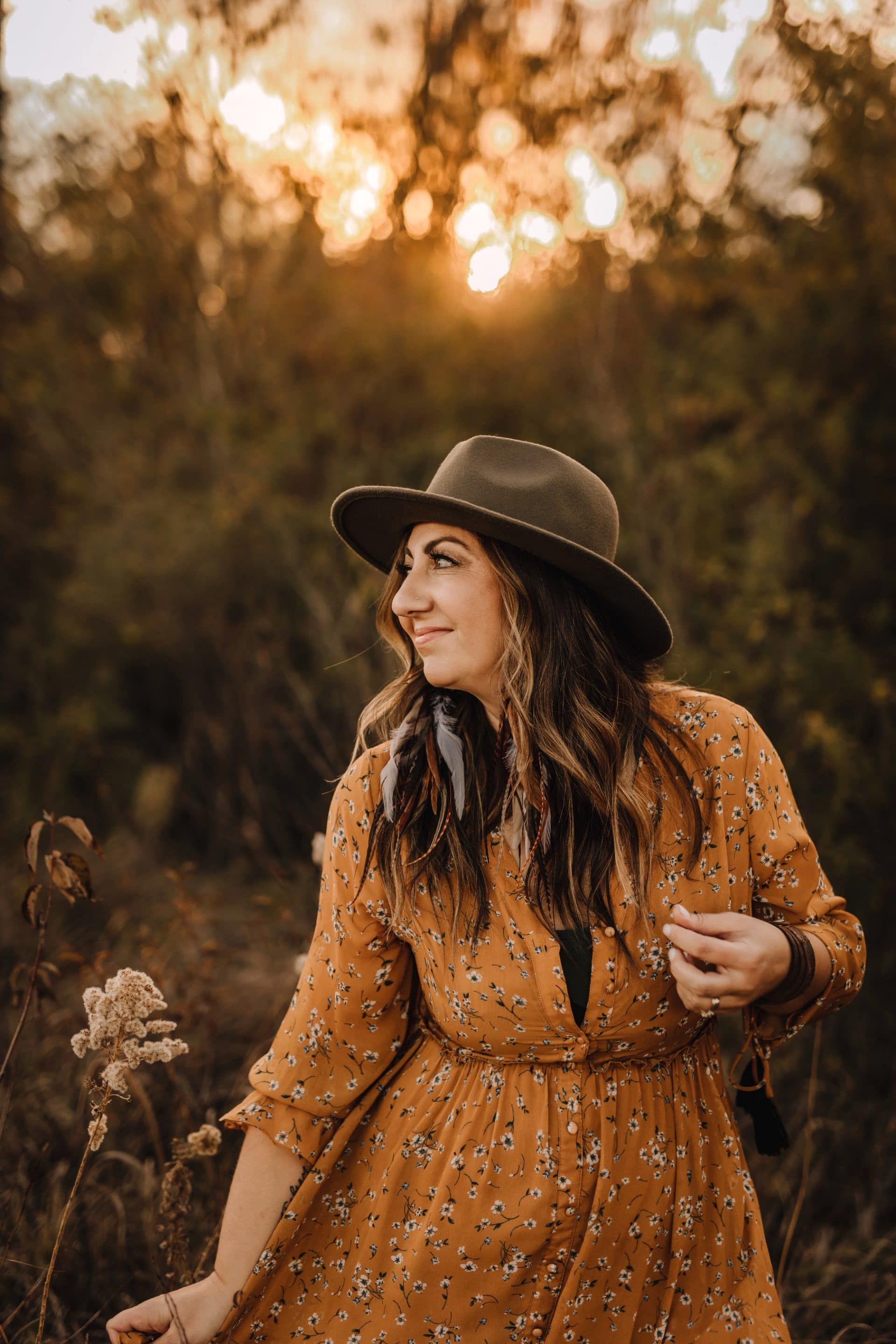 A woman in a dress and hat is standing in a field holding a flower.