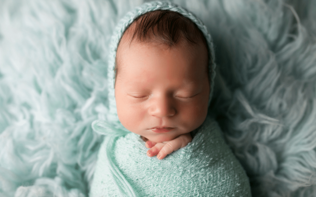 A newborn baby is wrapped in a blue blanket and wearing a hat.